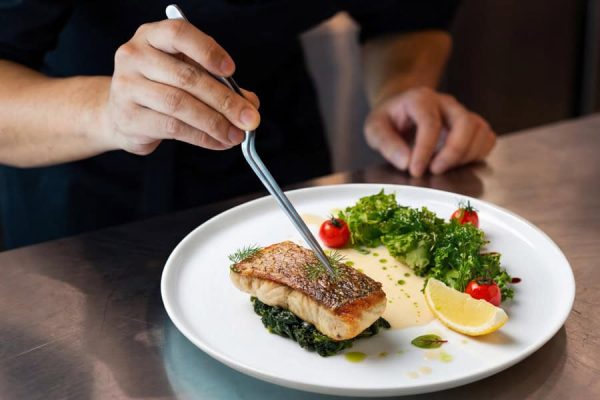 Chef finishing a plated fish dish with vegetables and lemon