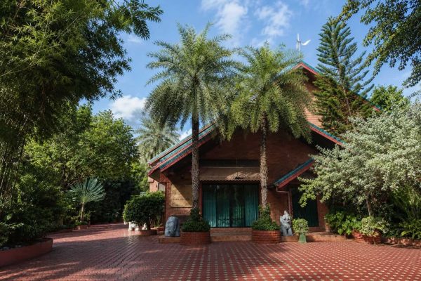 Traditional teak retreat house surrounded by tropical trees beneath a blue Bangkok sky