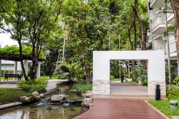 White garden arch and paved walkway beside water and tropical planting