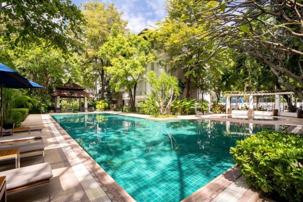 Turquoise outdoor pool surrounded by palms, flowering trees and shaded loungers