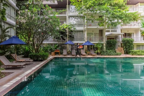 Outdoor swimming pool framed by trees, umbrellas and low-rise guest rooms