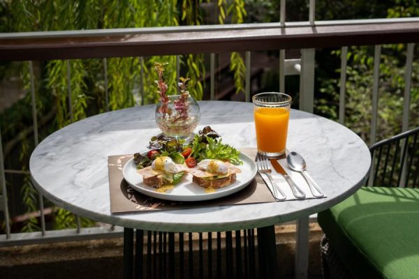 Breakfast plate, juice and coffee on a small table overlooking tropical greenery