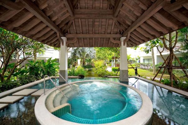 Round outdoor jacuzzi beneath a wooden pavilion in tropical gardens