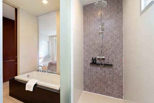 Dark wood kitchenette beside a bright bathroom and bathtub in apartment-style accommodation